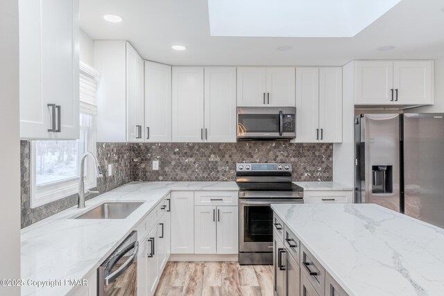 kitchen featuring sink, stainless steel appliances, white cabinetry, and light stone counters