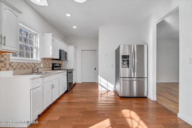 kitchen featuring appliances with stainless steel finishes, sink, white cabinets, backsplash, and light hardwood / wood-style flooring