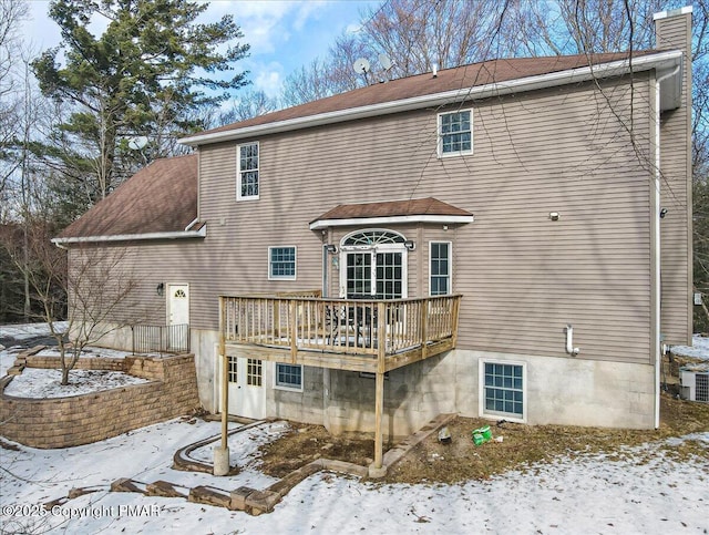 snow covered back of property with a wooden deck