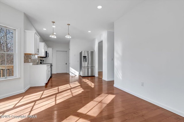 kitchen featuring stainless steel fridge with ice dispenser, hanging light fixtures, white cabinets, hardwood / wood-style floors, and backsplash