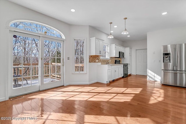 kitchen featuring stainless steel appliances, tasteful backsplash, white cabinets, decorative light fixtures, and light wood-type flooring