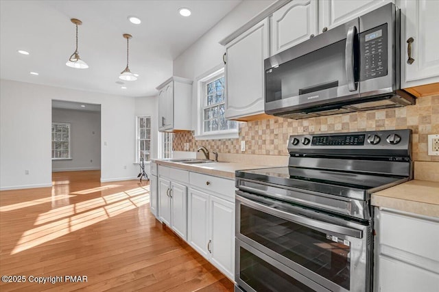 kitchen with sink, white cabinetry, light wood-type flooring, pendant lighting, and stainless steel appliances