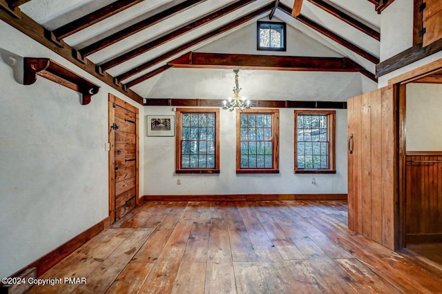 spare room with lofted ceiling with beams, an inviting chandelier, baseboards, and hardwood / wood-style floors