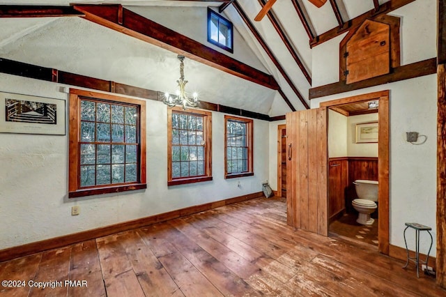 unfurnished room featuring lofted ceiling with beams, an inviting chandelier, wood-type flooring, and baseboards