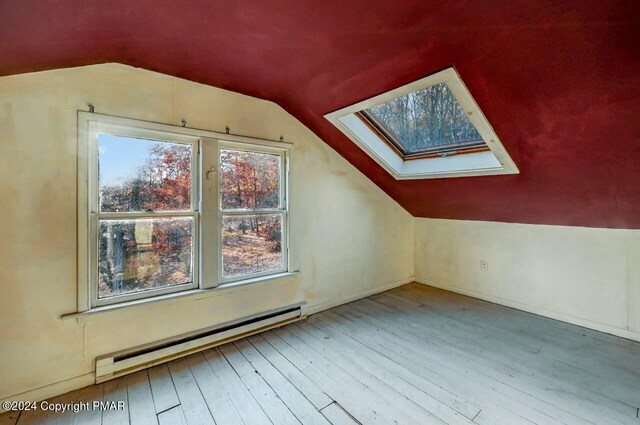 additional living space featuring a baseboard heating unit, vaulted ceiling with skylight, and hardwood / wood-style flooring