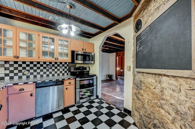 kitchen with decorative backsplash, tile countertops, dark floors, appliances with stainless steel finishes, and beam ceiling