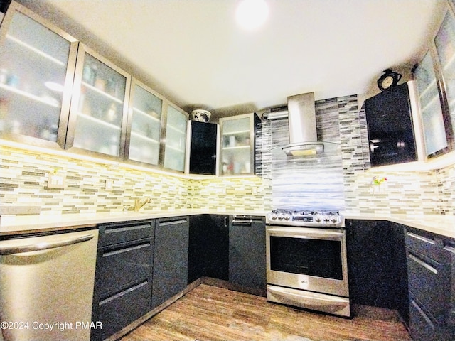 kitchen featuring wall chimney exhaust hood, sink, appliances with stainless steel finishes, light hardwood / wood-style floors, and backsplash