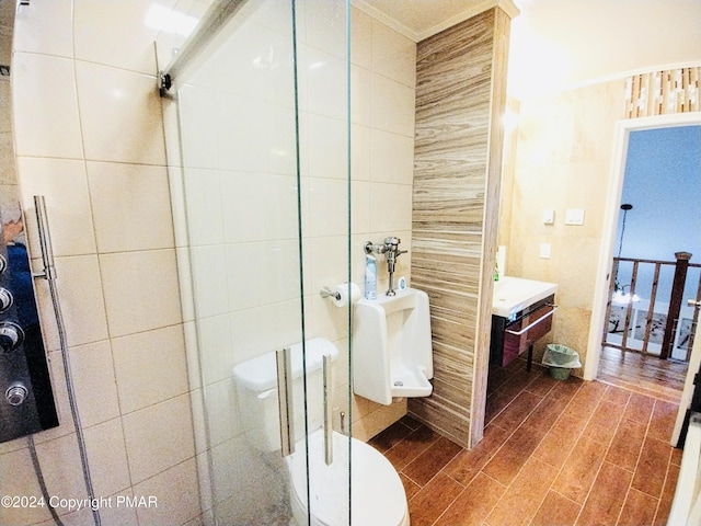 bathroom featuring tile walls, hardwood / wood-style flooring, ornamental molding, walk in shower, and toilet