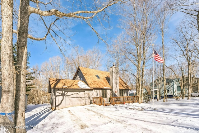 view of snowy exterior featuring a garage, a chimney, and a wooden deck