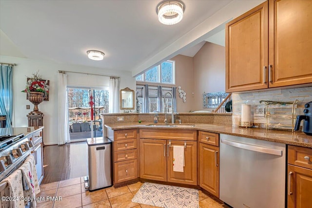 kitchen with light stone counters, stainless steel appliances, a peninsula, a sink, and backsplash