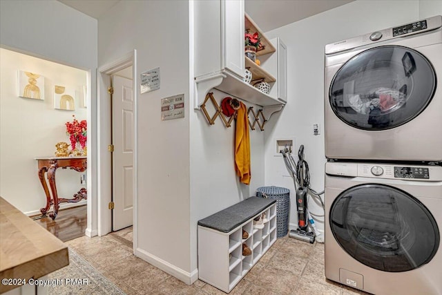 clothes washing area featuring laundry area, stacked washing maching and dryer, and baseboards