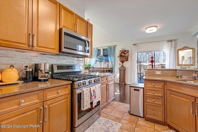 kitchen with light stone counters, light tile patterned flooring, a sink, appliances with stainless steel finishes, and tasteful backsplash