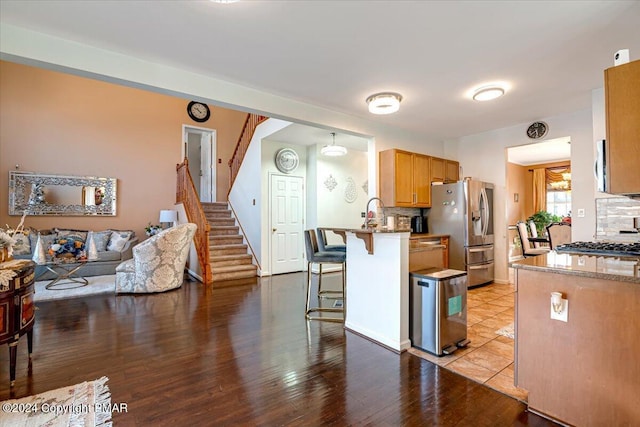 kitchen with light stone counters, light wood-style flooring, a breakfast bar, appliances with stainless steel finishes, and decorative backsplash