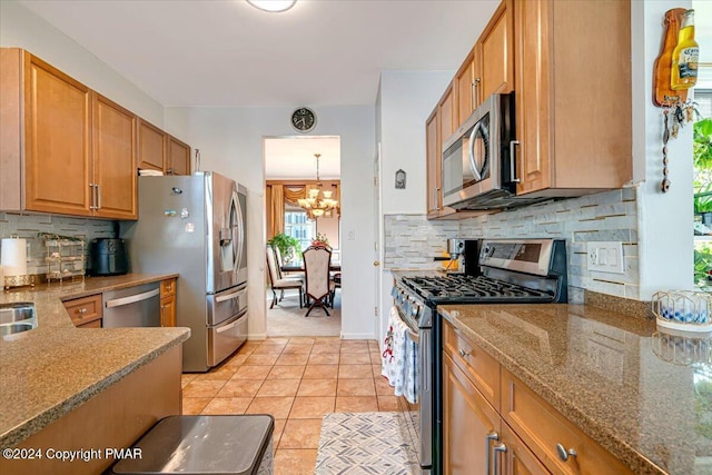 kitchen with brown cabinets, stainless steel appliances, decorative backsplash, light tile patterned flooring, and a chandelier