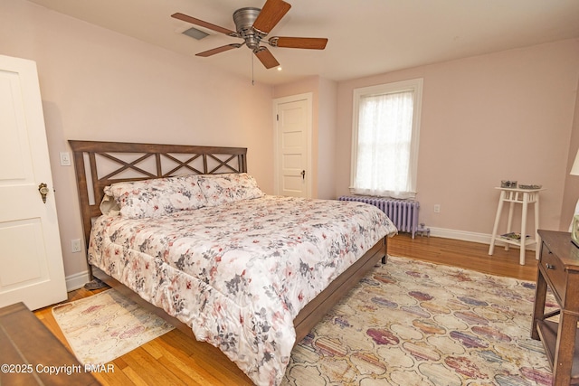 bedroom with baseboards, visible vents, a ceiling fan, radiator, and wood finished floors