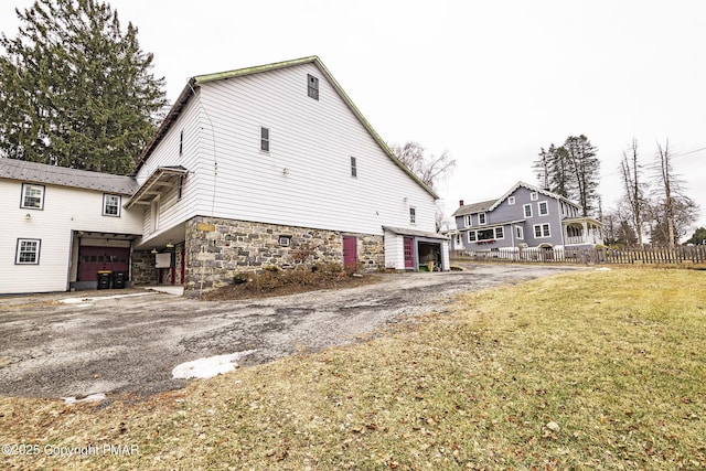 view of property exterior with driveway, a yard, an outdoor structure, and fence