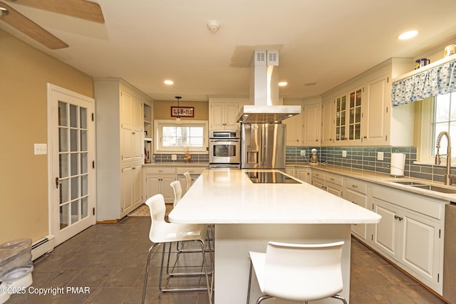 kitchen with island range hood, a sink, appliances with stainless steel finishes, a center island, and tasteful backsplash