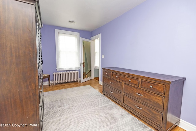 bedroom with baseboards, light wood-type flooring, visible vents, and radiator