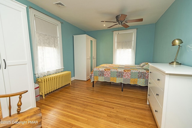 bedroom featuring a ceiling fan, light wood-type flooring, radiator, and visible vents