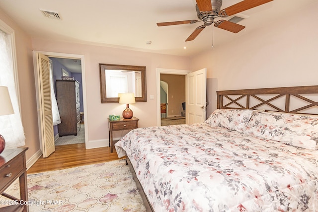 bedroom with arched walkways, a ceiling fan, baseboards, visible vents, and light wood-style floors