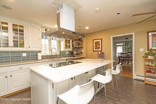 kitchen featuring black electric stovetop, a sink, decorative backsplash, a center island, and island exhaust hood