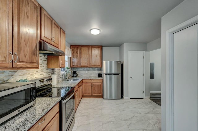 kitchen with under cabinet range hood, light stone counters, electric panel, a sink, and appliances with stainless steel finishes