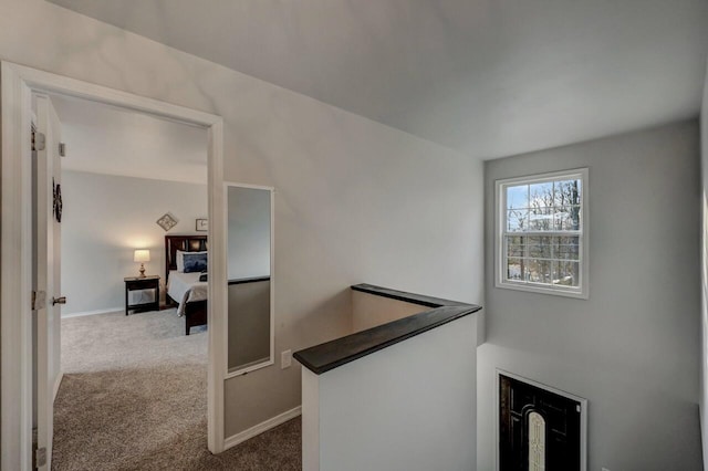 hall with an upstairs landing, baseboards, and carpet floors