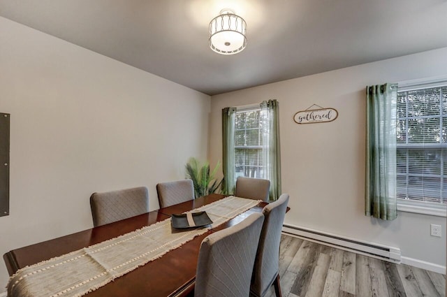 dining space featuring a baseboard heating unit, wood finished floors, and baseboards