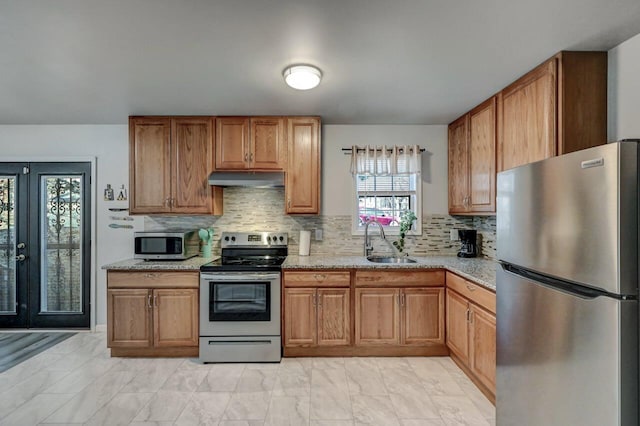 kitchen with under cabinet range hood, light stone counters, a sink, french doors, and appliances with stainless steel finishes