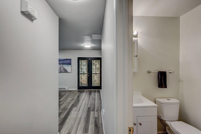 half bathroom with french doors, toilet, wood finished floors, and vanity