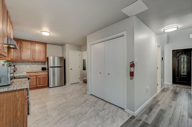 kitchen featuring backsplash, baseboards, electric panel, freestanding refrigerator, and brown cabinetry