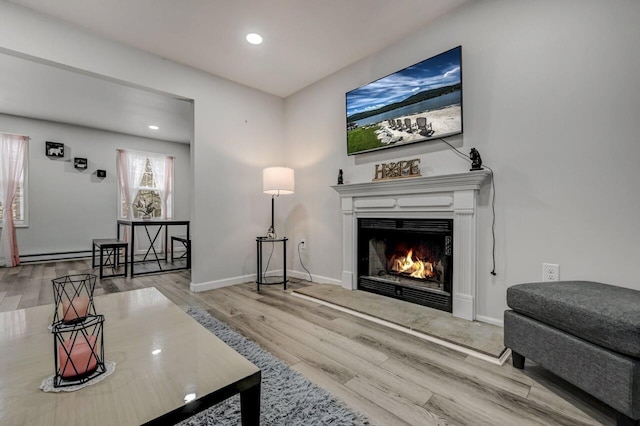 living area with a baseboard heating unit, baseboards, a lit fireplace, recessed lighting, and wood finished floors