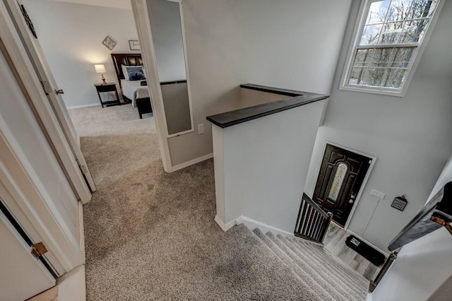 hall with an upstairs landing, baseboards, and carpet floors