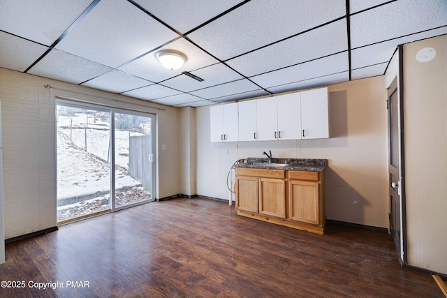 kitchen featuring a sink, dark countertops, a drop ceiling, and dark wood-style flooring