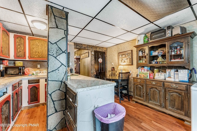 kitchen featuring light wood-type flooring, light countertops, a peninsula, and a drop ceiling