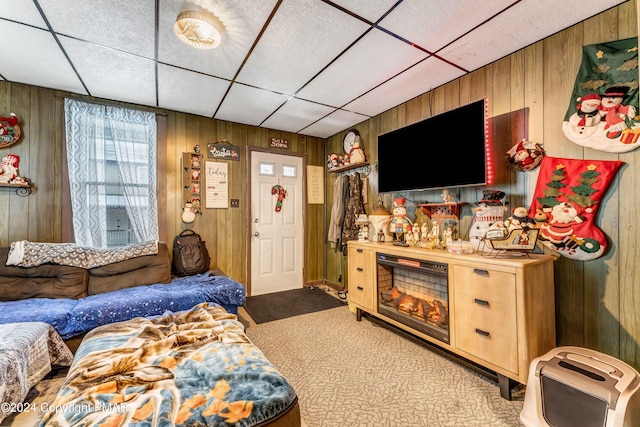 carpeted living area with a drop ceiling and wood walls