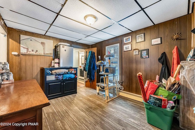 interior space featuring a paneled ceiling, wooden walls, a baseboard heating unit, and wood finished floors