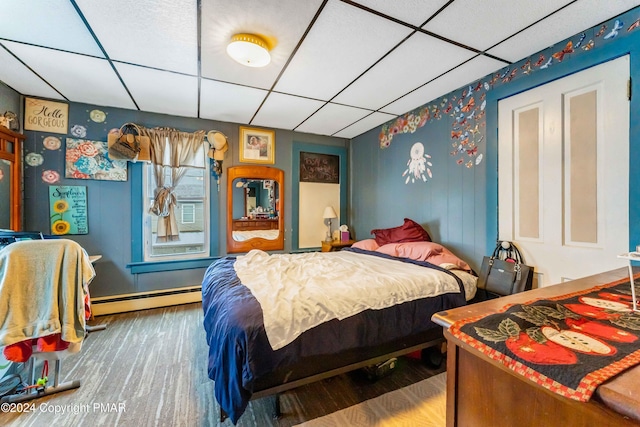 bedroom featuring baseboard heating, wood finished floors, and a paneled ceiling