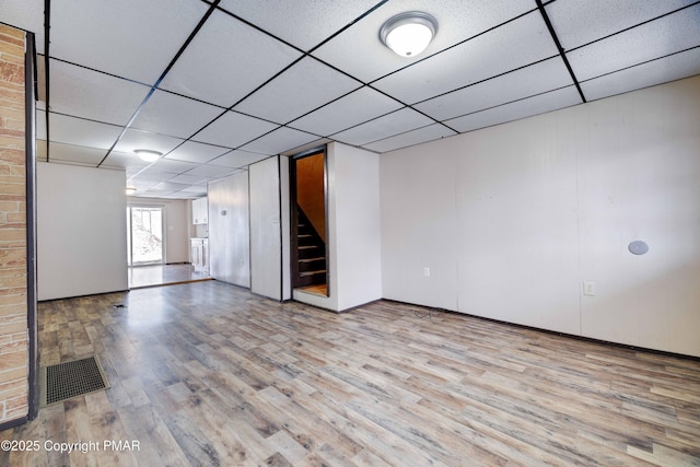 basement with stairway, a drop ceiling, visible vents, and wood finished floors