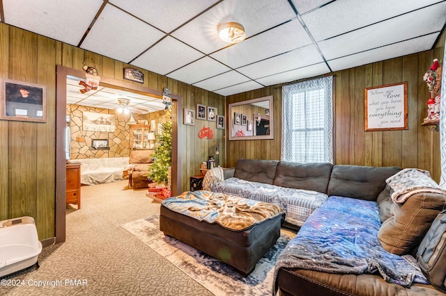 carpeted living area featuring wooden walls and a drop ceiling