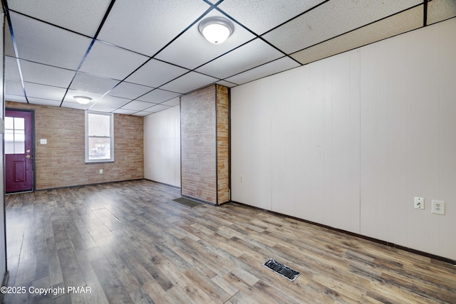 empty room featuring a paneled ceiling, wood-type flooring, and brick wall