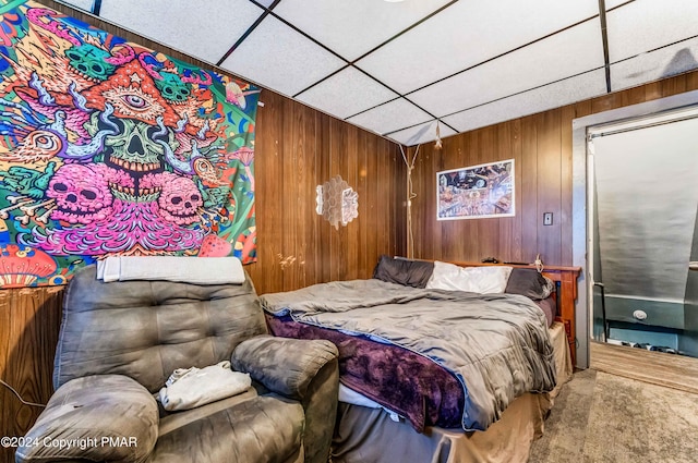 carpeted bedroom featuring a paneled ceiling and wood walls