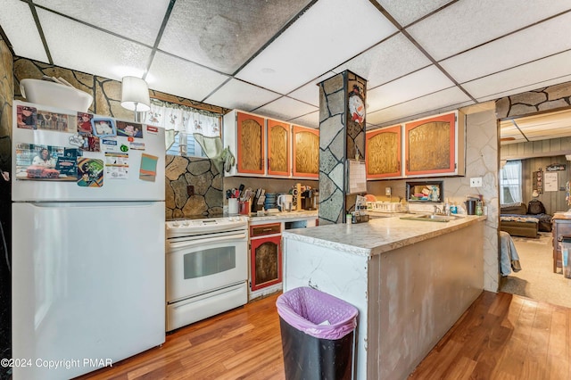 kitchen featuring a peninsula, white appliances, light wood-style floors, and a paneled ceiling