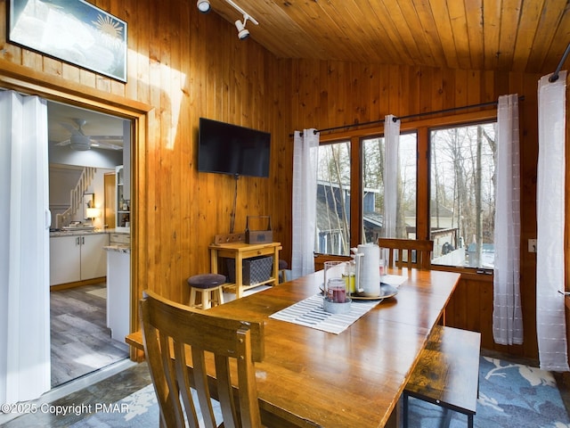 dining space featuring rail lighting, vaulted ceiling, wooden ceiling, and wooden walls