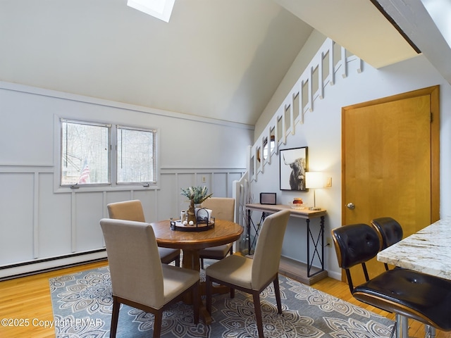 dining space with a baseboard heating unit, light hardwood / wood-style flooring, and vaulted ceiling with skylight