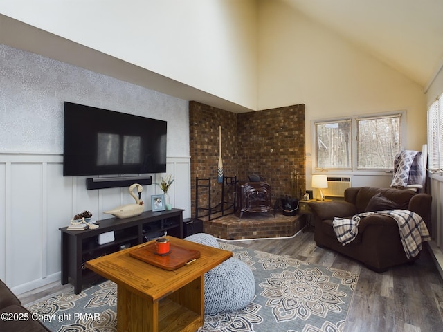 living room with hardwood / wood-style flooring, a wood stove, a wall mounted AC, and high vaulted ceiling