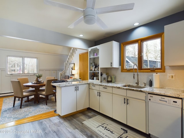 kitchen with sink, light hardwood / wood-style flooring, dishwasher, light stone countertops, and kitchen peninsula