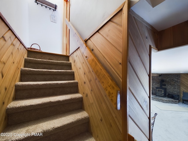 staircase with carpet floors, a wood stove, and wooden walls