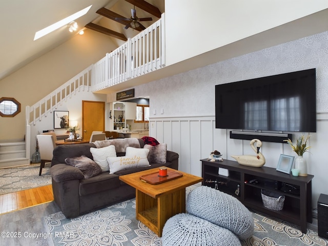 living room featuring high vaulted ceiling, a skylight, beamed ceiling, hardwood / wood-style flooring, and ceiling fan