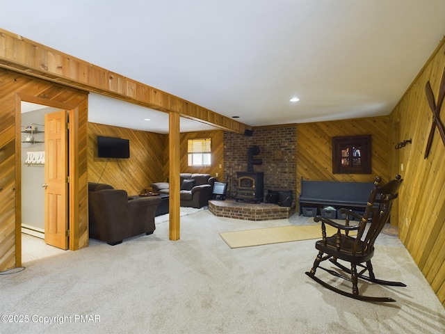 living room featuring a baseboard radiator, a wood stove, light colored carpet, and wood walls